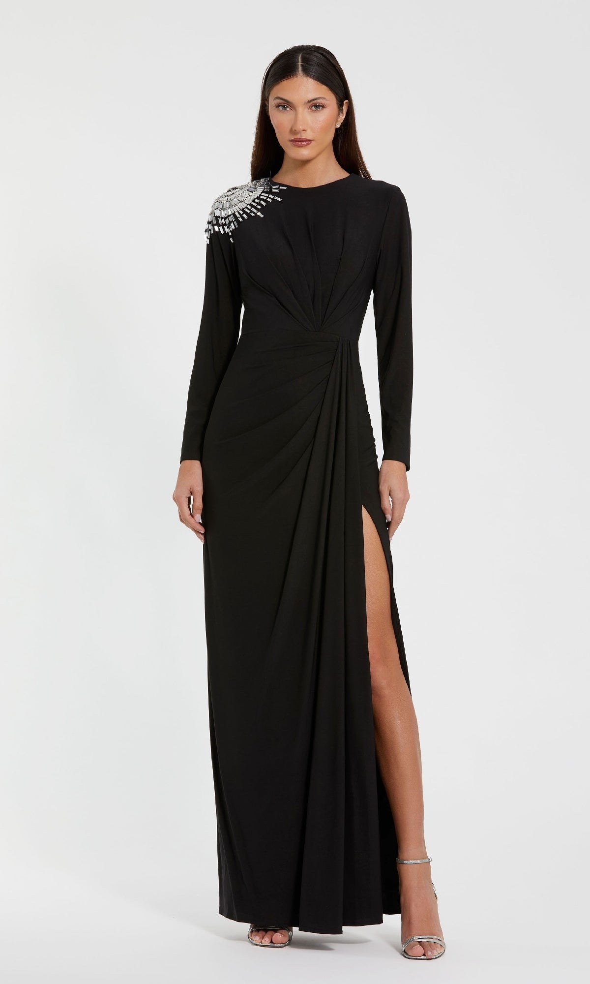 A woman wearing the Mac Duggal 44136 long formal dress, featuring a high slit and crystal beading on one shoulder, stands against a plain white background.